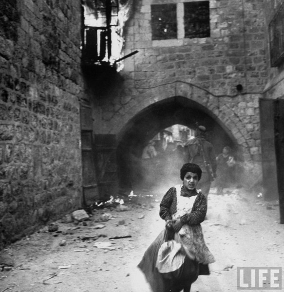 Jewish girl, Rachel Levy, 7, fleeing from street w. burning bldgs. as the Arabs sack Jerusalem after its surrender. May 28, 1948. John Phillips
